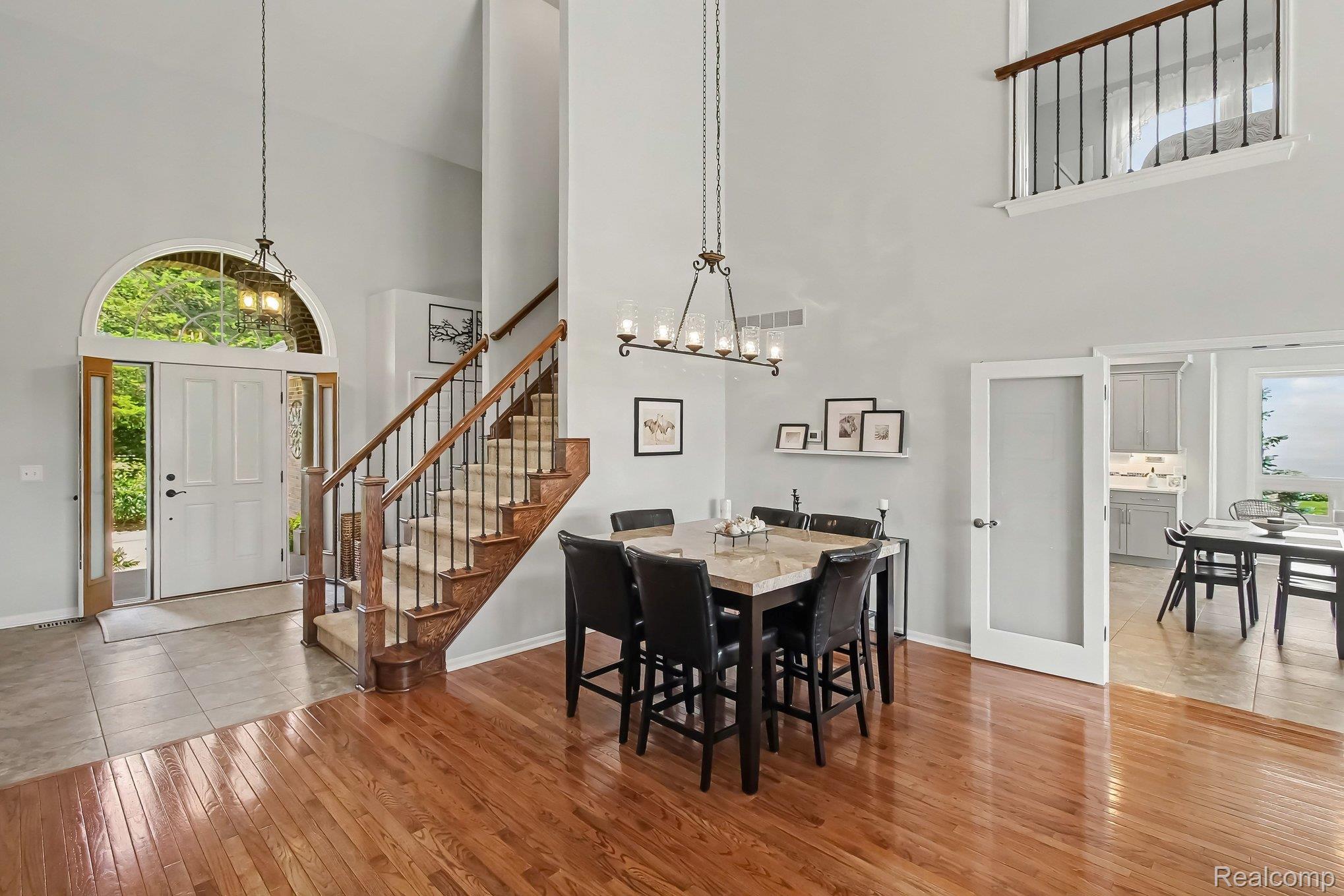 Foyer and dining area with an arched entry window, wood staircase, vaulted ceiling, and hardwood floors.