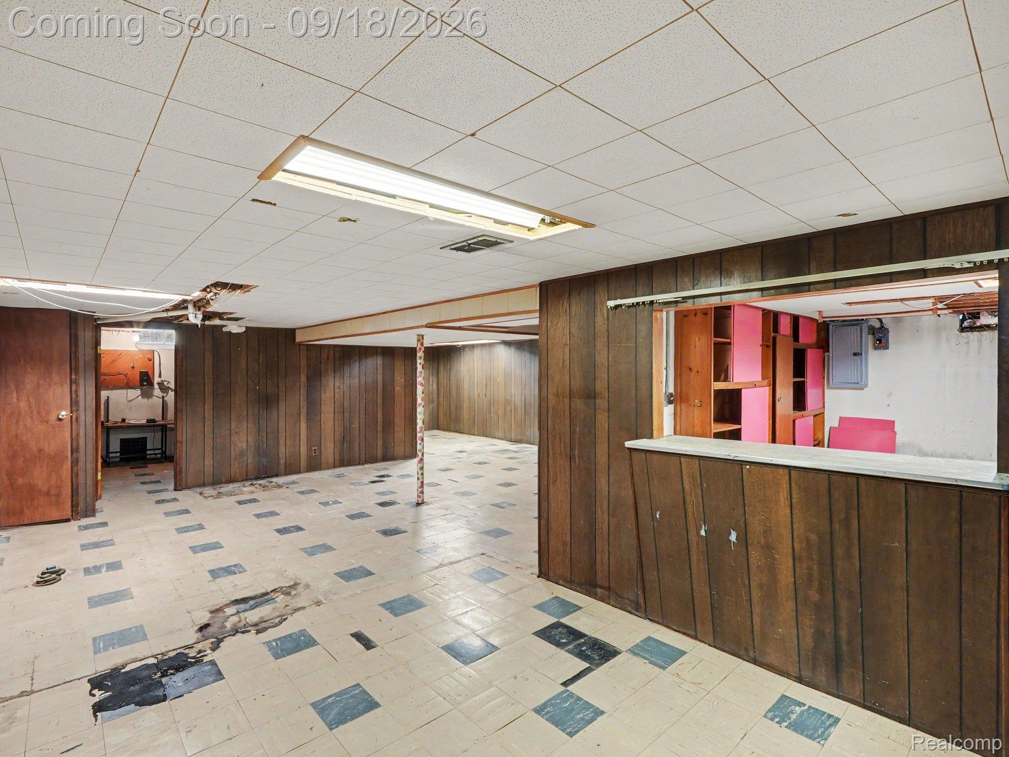 Vacant basement with wood paneling, a tiled floor, and a built-in counter and shelving.