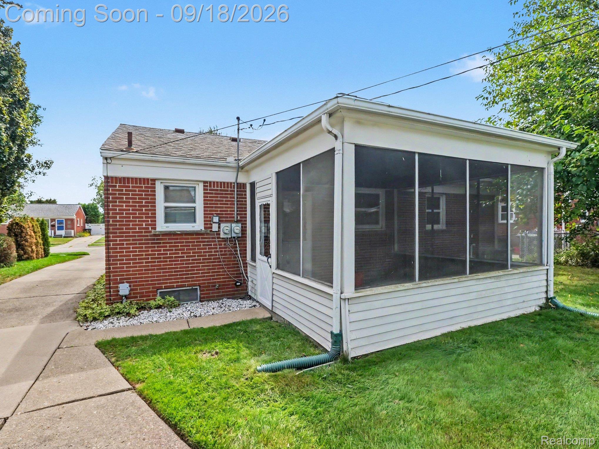 Rear exterior of a brick house with a large screened porch and lawn.