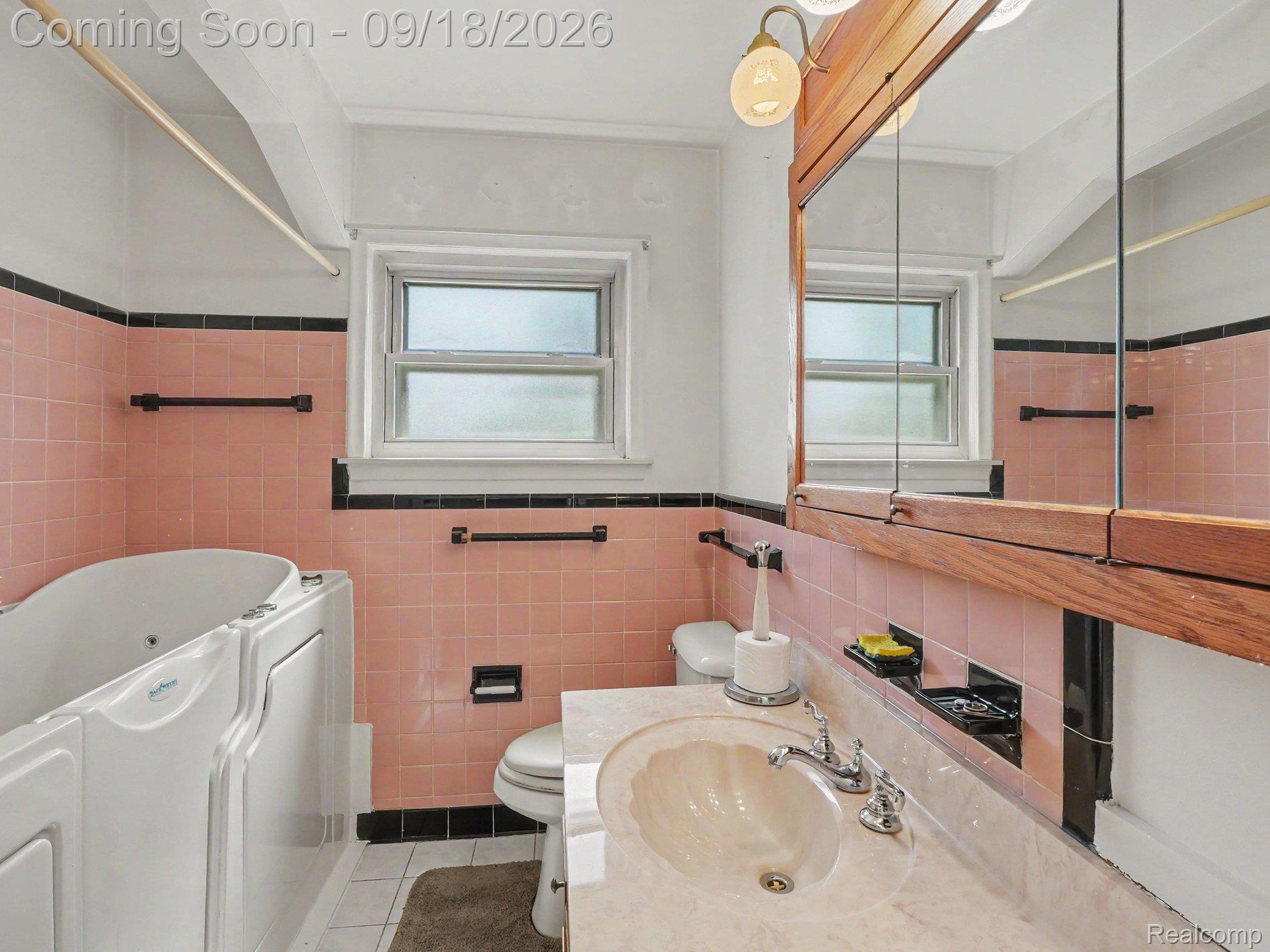 Bathroom with pink tile, a white jetted tub, and a marble-look vanity beneath a large mirror.