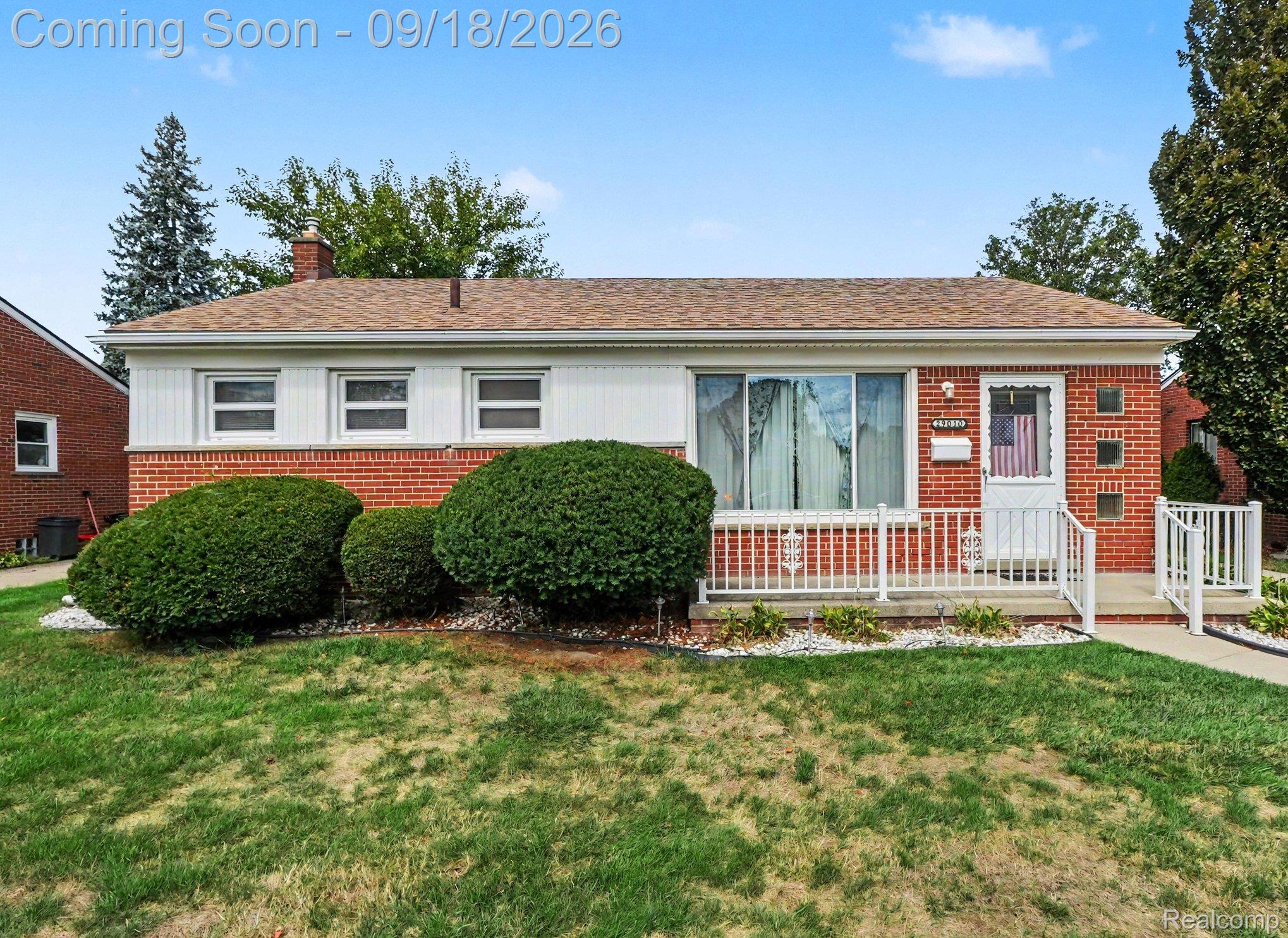 Red-brick ranch house with white siding, trimmed shrubs, and a white-railed front porch.