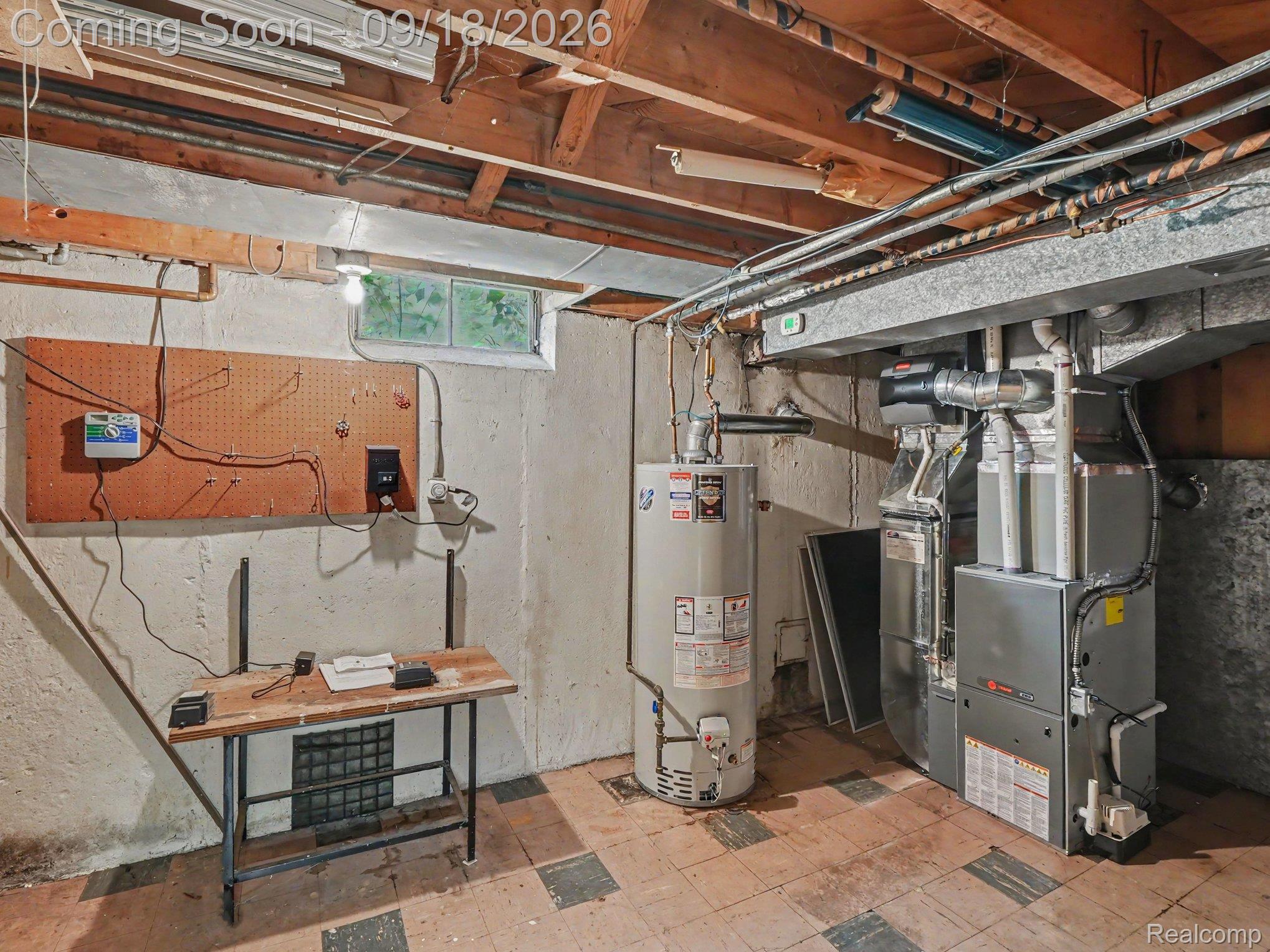 Unfinished basement utility room with exposed ceiling joists, furnace, water heater, and workbench.