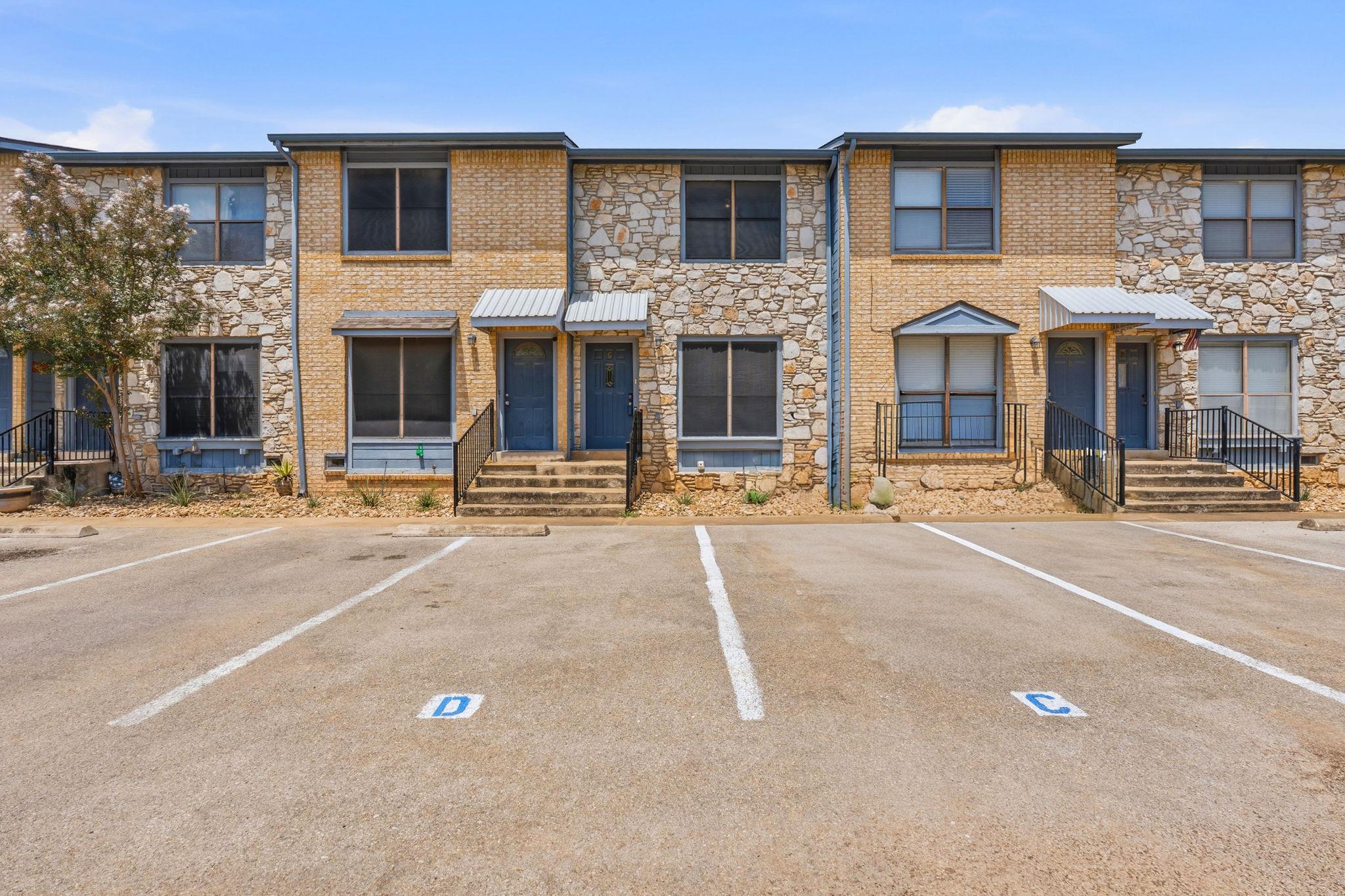 Row of brick and stone townhomes with blue doors and parking spaces in front.