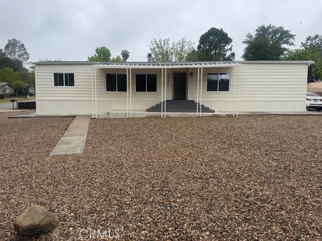 Single-story manufactured home with a covered porch, gravel yard, and concrete walkway.