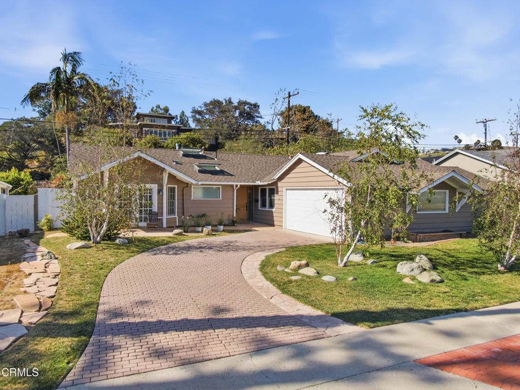 Tan single-story house with an attached garage and curved brick-paver driveway.