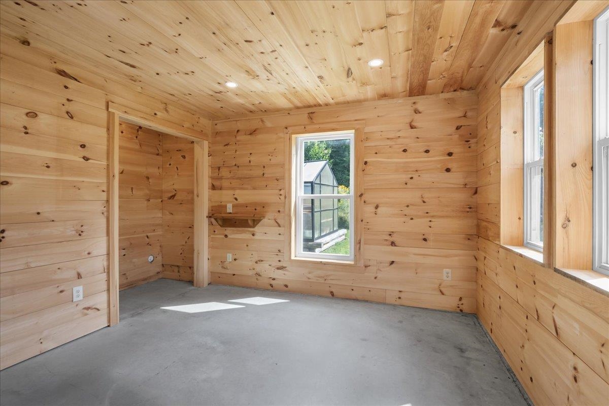 Unfinished pine-lined room with a concrete floor and several windows.