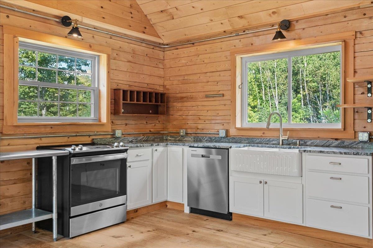 Kitchen with white cabinets, stainless steel appliances, and wood-paneled walls overlooking trees.