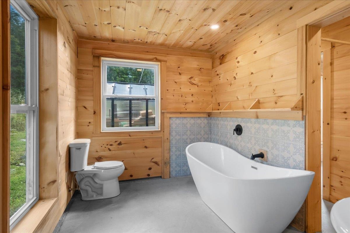 Bathroom with a freestanding tub, blue patterned tile, and knotty pine walls and ceiling.