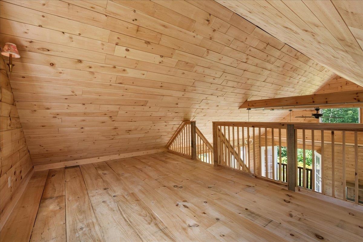Wood-finished loft with a sloped plank ceiling and railing overlooking the floor below.