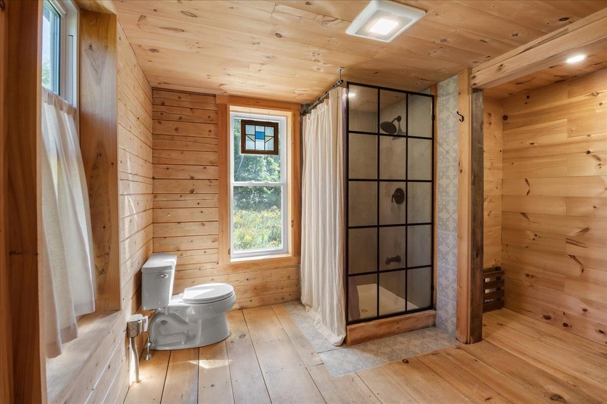 Wood-paneled bathroom with a black-framed glass shower and stained-glass window accent.