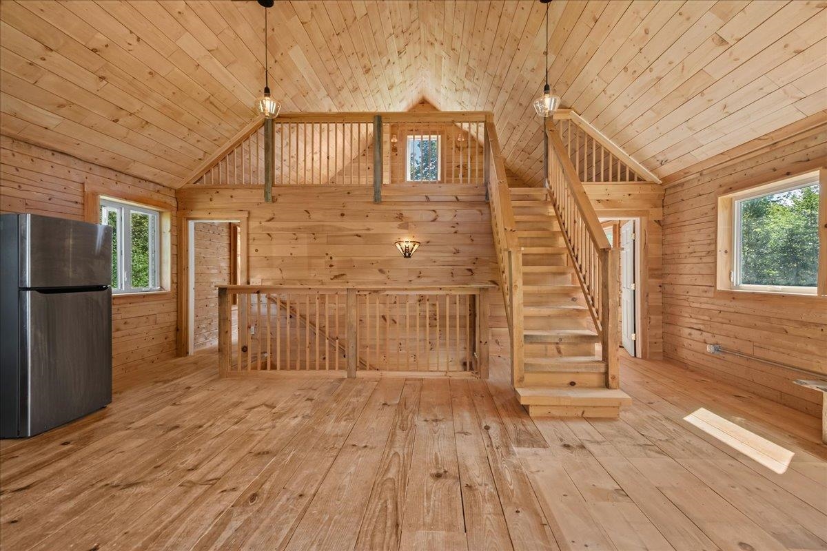 Unfurnished wood-paneled room with a vaulted ceiling, loft, and central staircase.