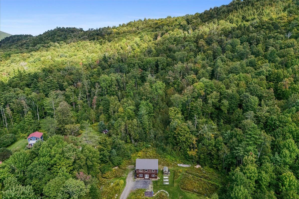 Aerial view of a home surrounded by dense woods, with forested hills in the background.