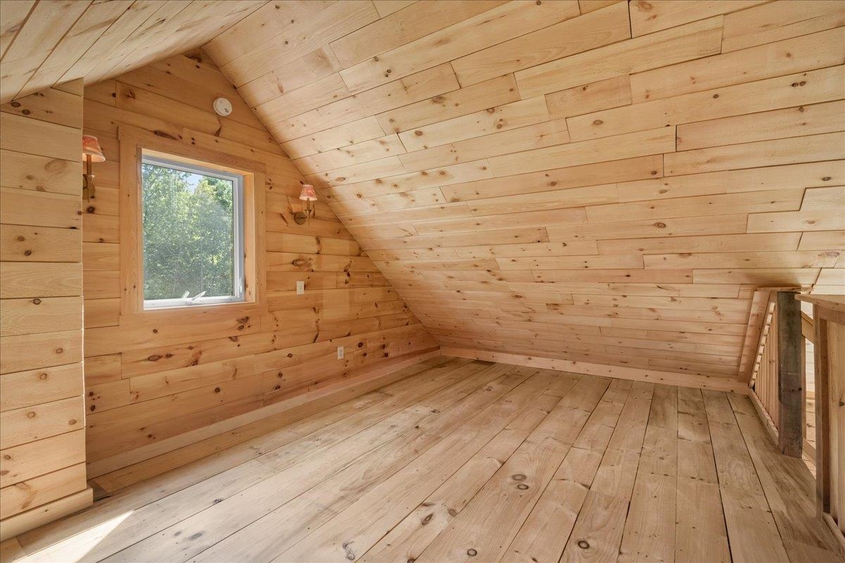 Vacant wood-paneled attic loft with a sloped ceiling, window, and wooden railing.