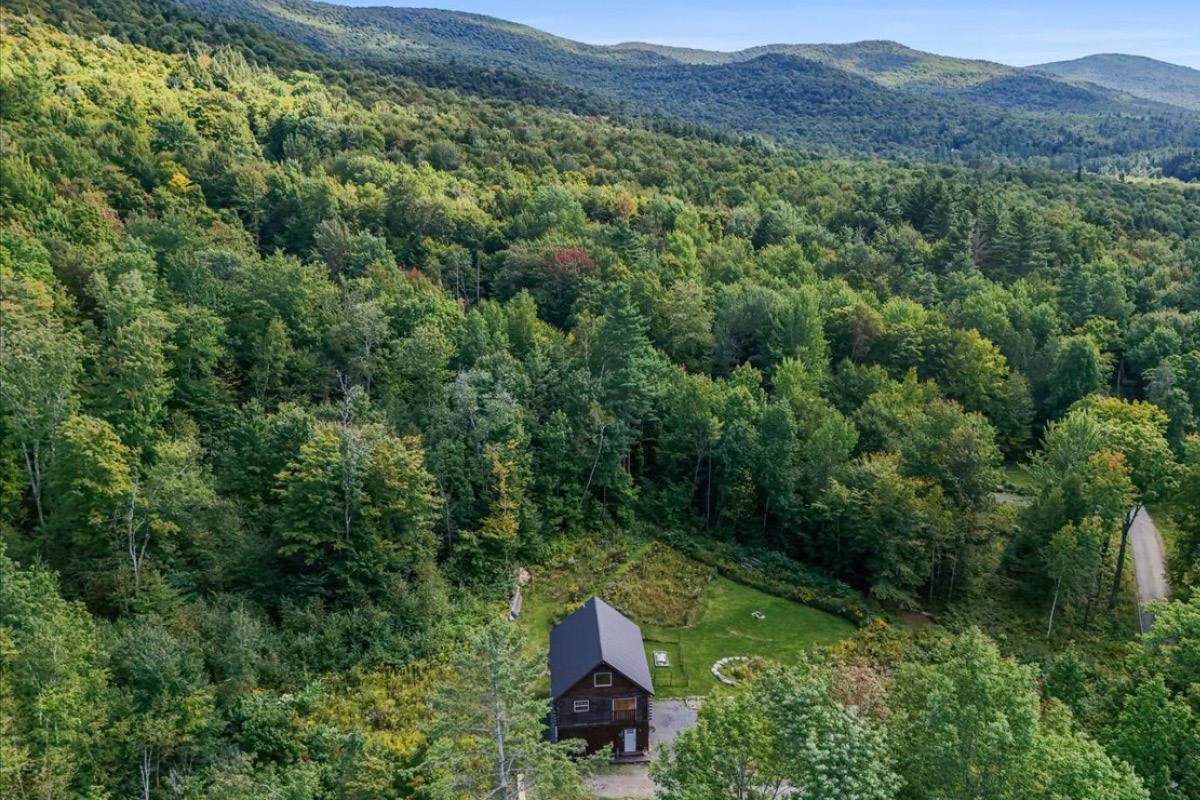 Aerial view of a house and lawn surrounded by forest, with mountain ridges in the distance.
