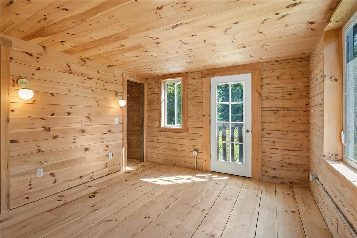 Empty wood-paneled room with plank ceiling and floor, wall sconces, and a glass-paneled door.