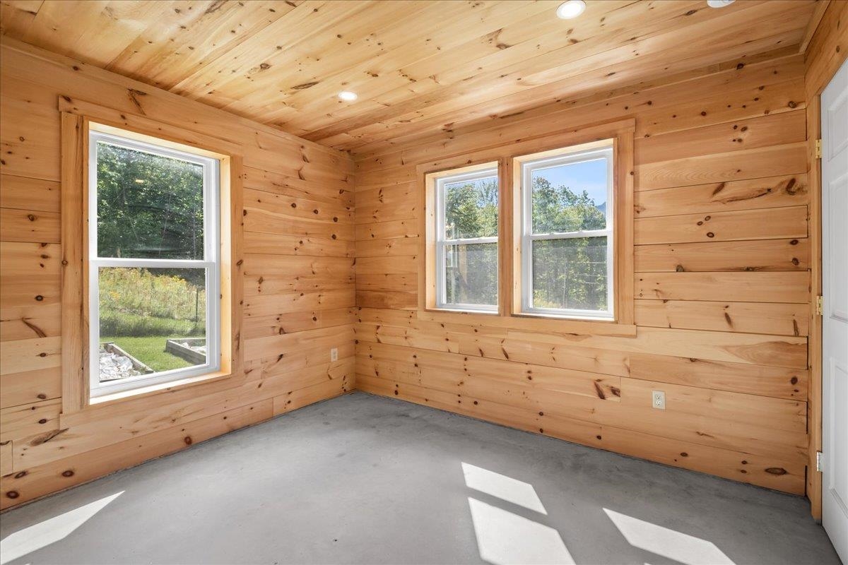 Empty wood-paneled room with a concrete floor and three windows.