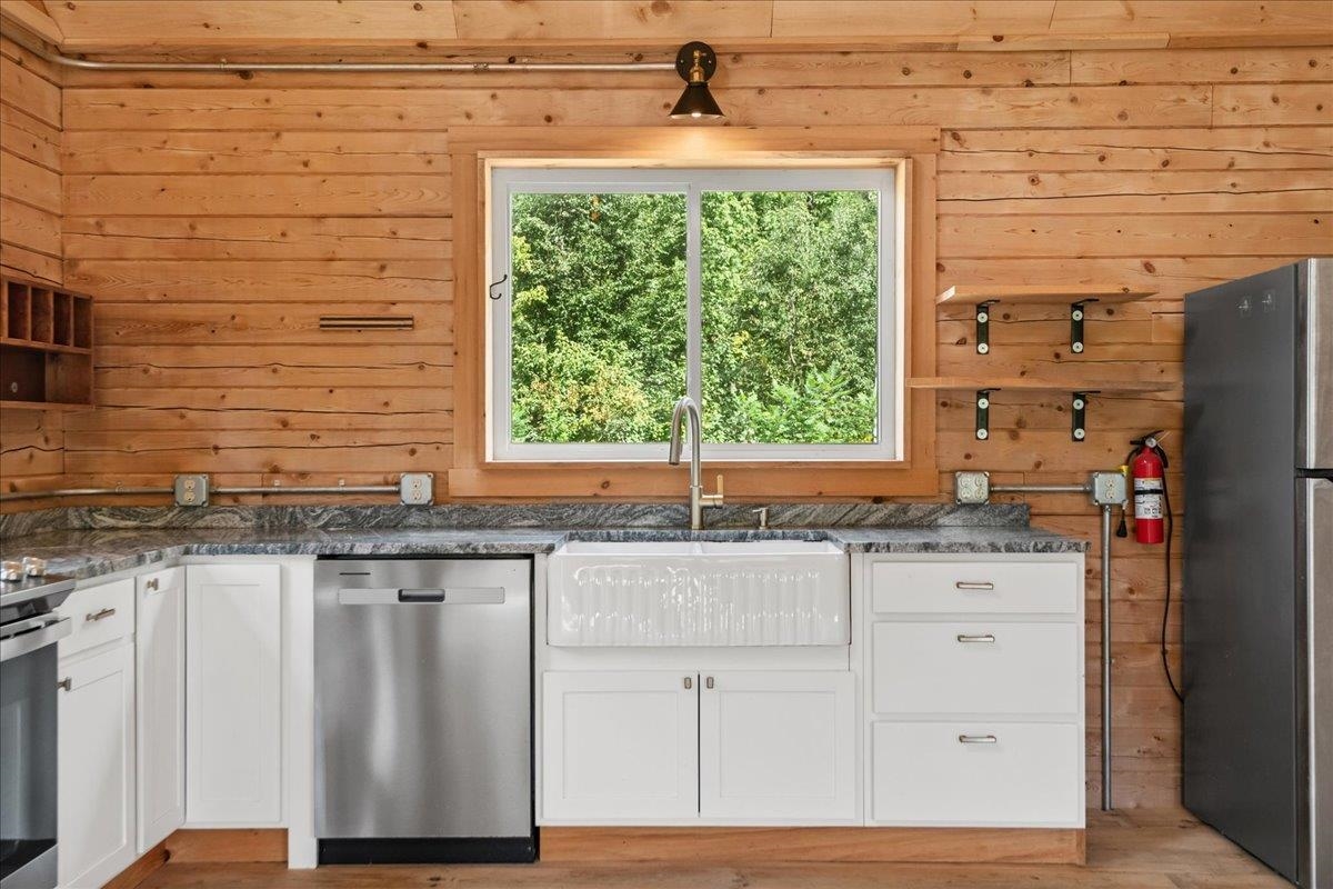 Kitchen with a farmhouse sink, white cabinets, and warm wood plank walls.