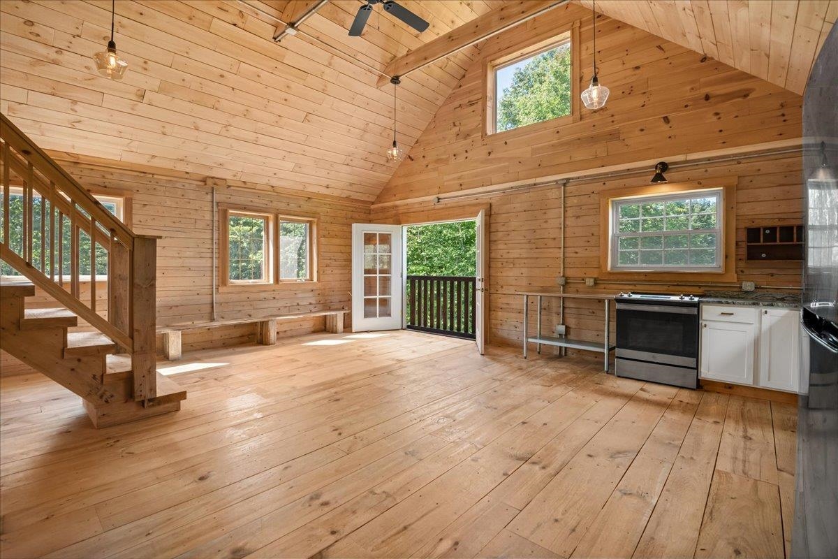 Vacant wood-paneled kitchen with vaulted ceiling, staircase, and open door to a balcony.