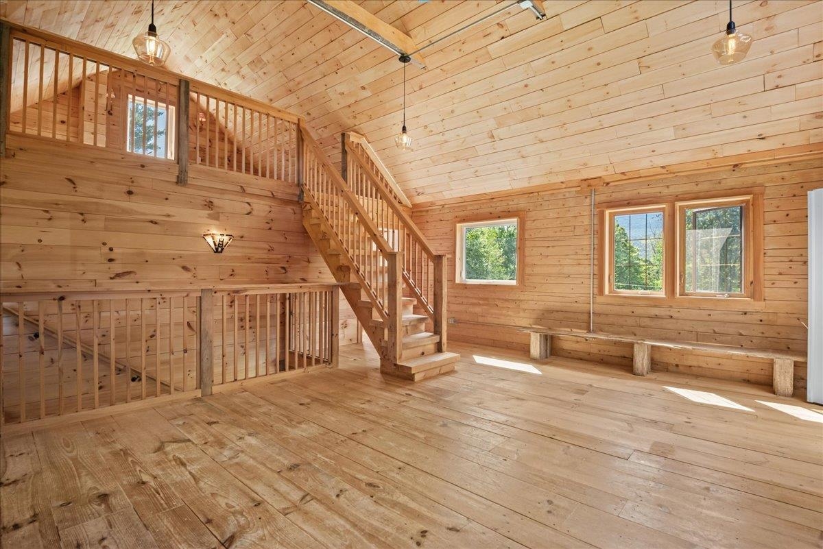 Wood-paneled open room with a high ceiling, loft staircase, and built-in bench beneath the windows.