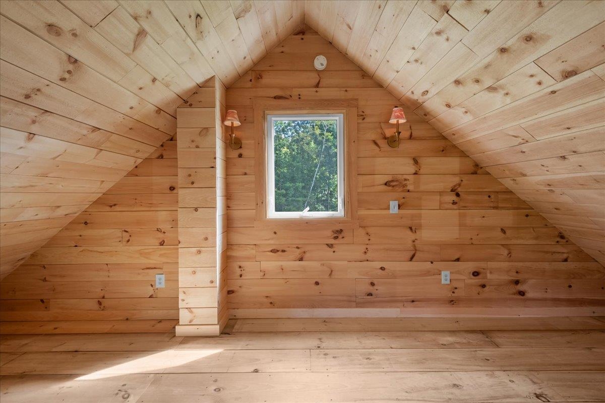 Unfurnished wood-paneled attic room with a small window and steeply sloped ceiling.