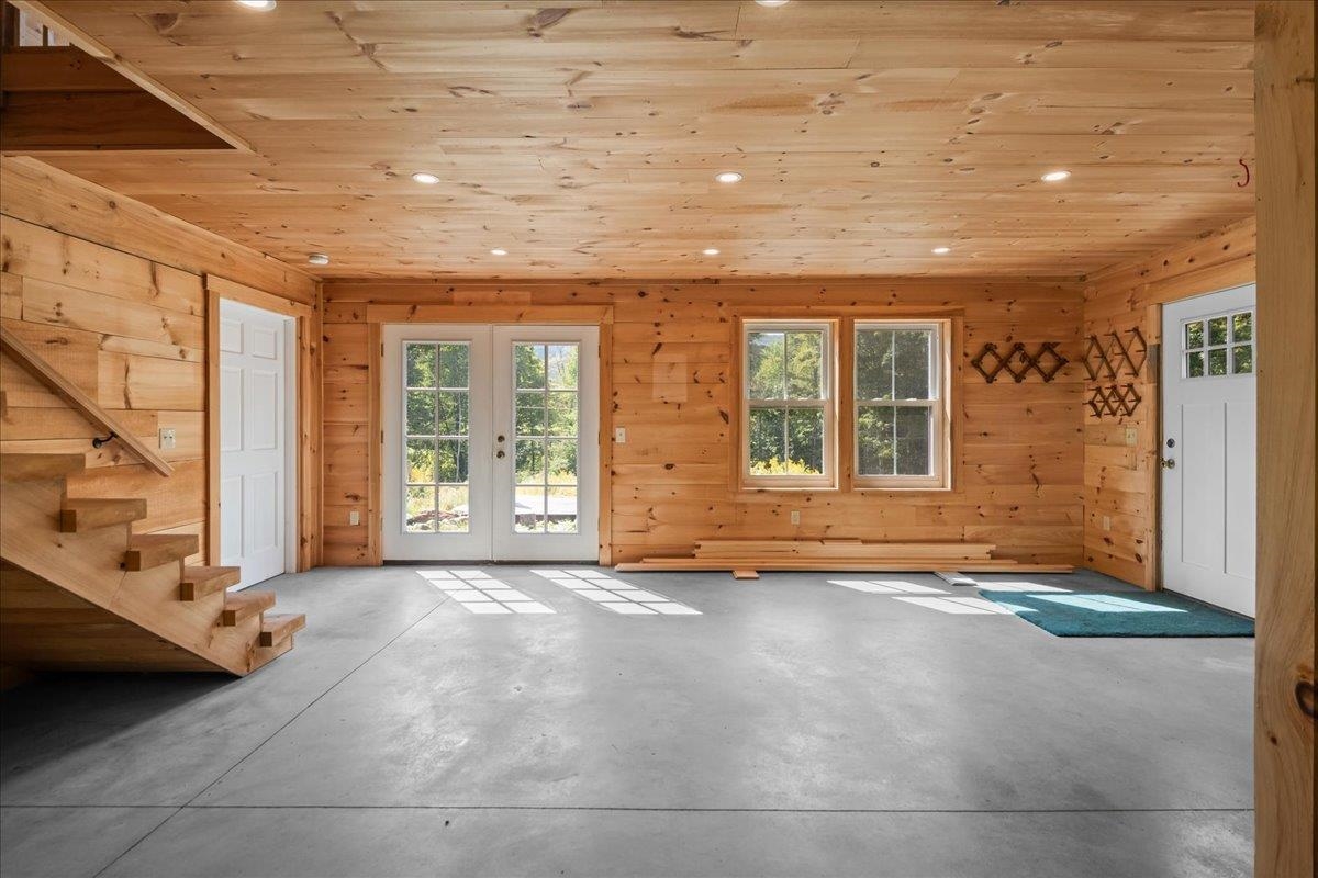 Vacant wood-paneled interior with a concrete floor, staircase, and glazed double doors.