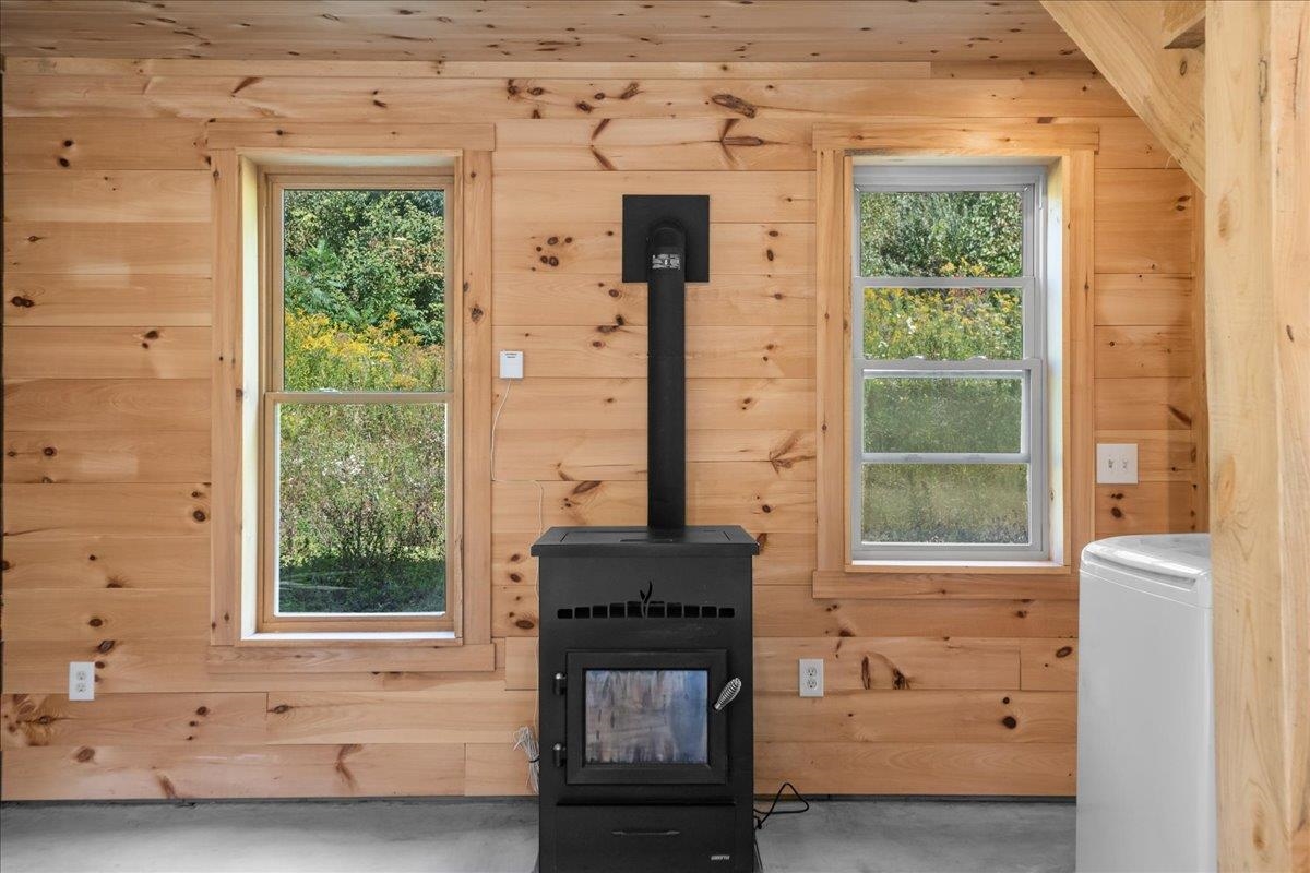 Unfurnished wood-paneled room with a black wood stove between two windows.