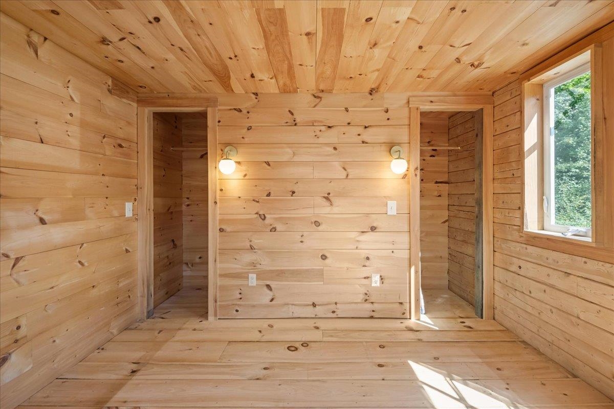 Empty knotty-pine room with two lit sconces and a sunlit window.