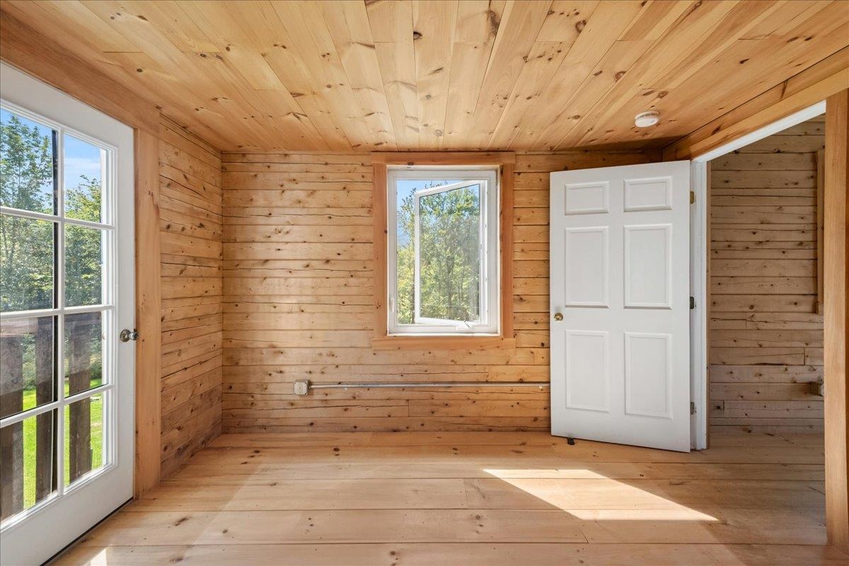Vacant wood-paneled room with a glazed door, central window, and open white door.