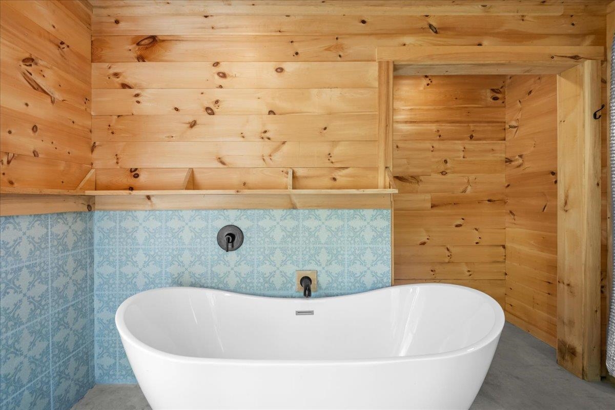 Bathroom with a white freestanding tub, blue patterned tile, and warm wood walls.