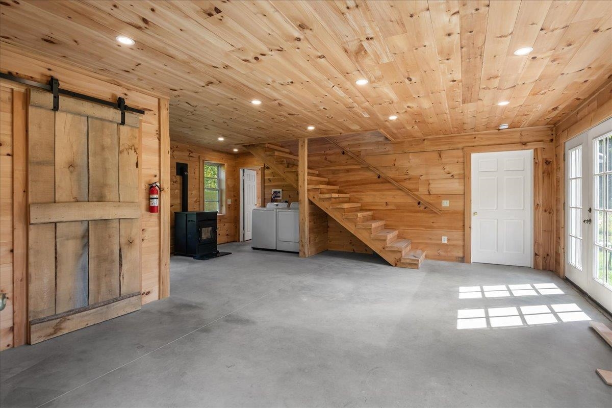 Wood-paneled garage with concrete floor, sliding barn door, staircase, wood stove, and washer and dryer.