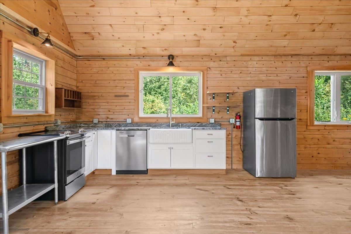 Wood-paneled kitchen with white cabinets, stainless steel appliances, and windows overlooking trees.