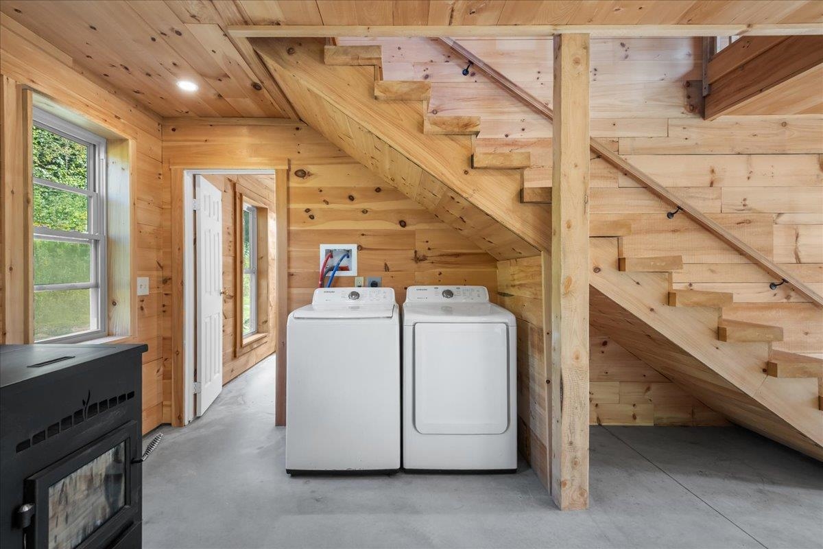 Laundry area beneath a wooden staircase, with a washer and dryer and knotty wood paneling.