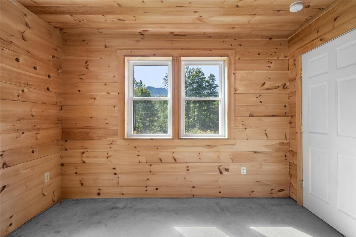 Empty pine-paneled room with two windows overlooking trees and a distant mountain.