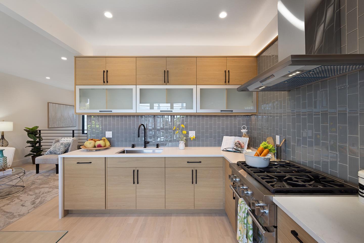 Modern kitchen with light wood cabinets, gray tile backsplash, and a large stainless-steel gas range.