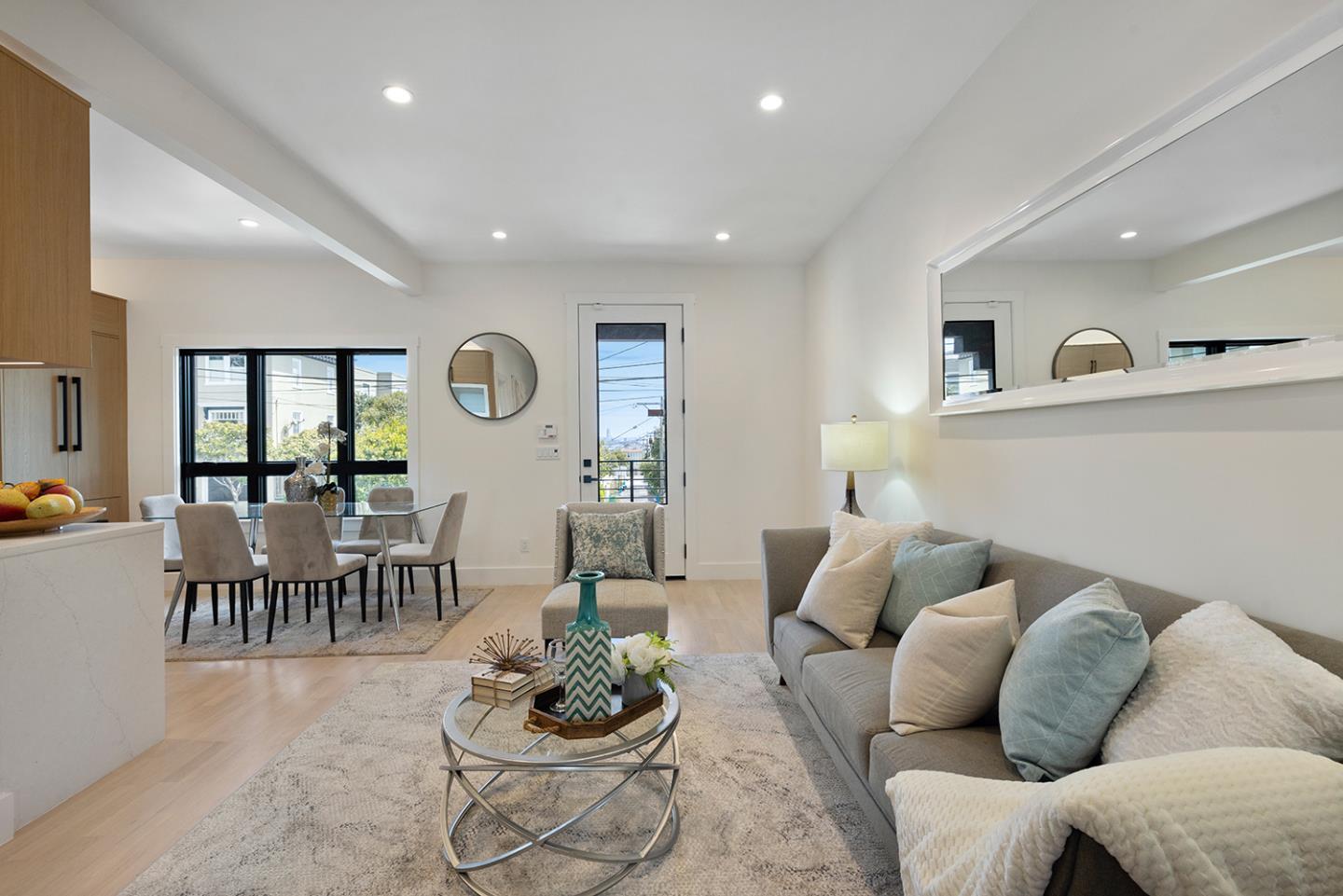 Staged living and dining room with a gray sofa, glass coffee table, and large windows.