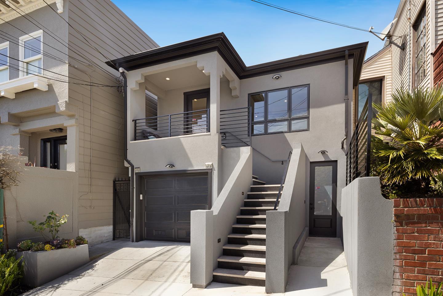 Gray two-story home with a front balcony, central stairs, garage, and separate entry.
