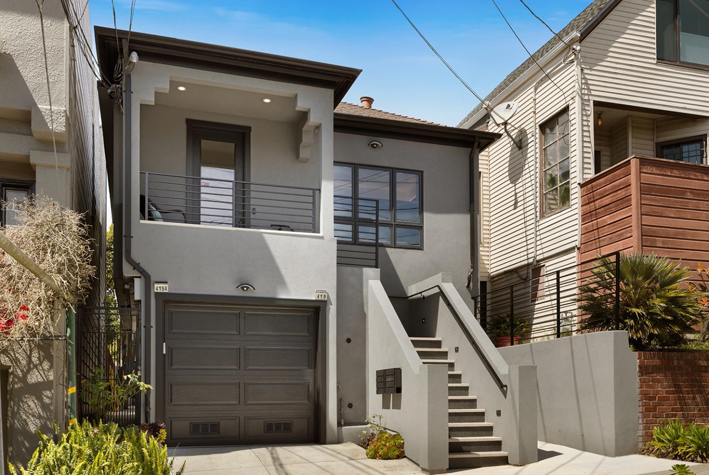 Modern gray stucco home with a garage, upper balcony, and exterior stairs.