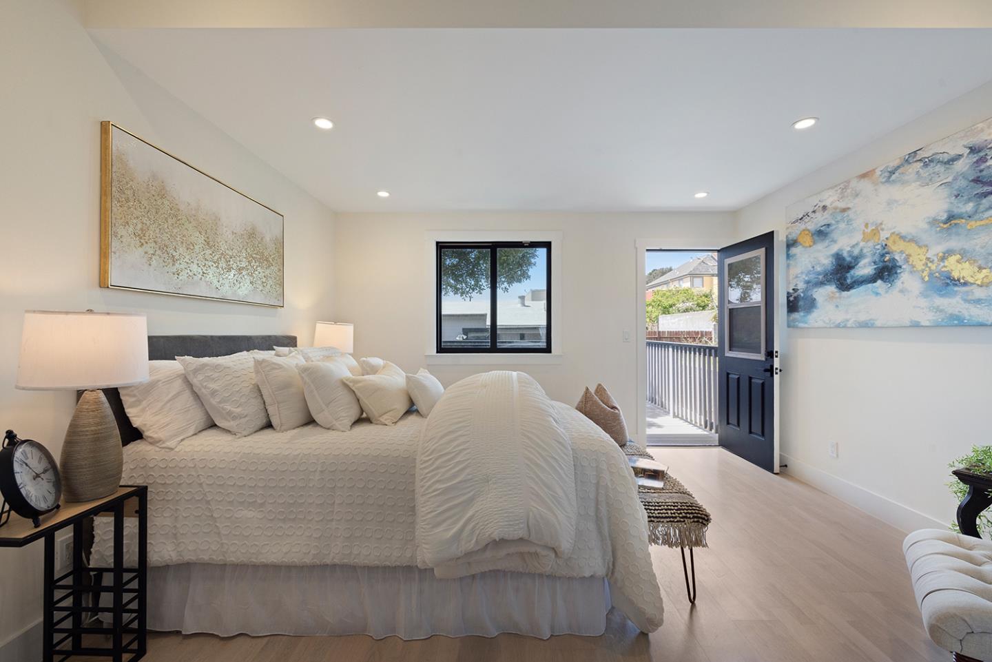 Staged bedroom with white bedding, abstract wall art, and an open door to a balcony.