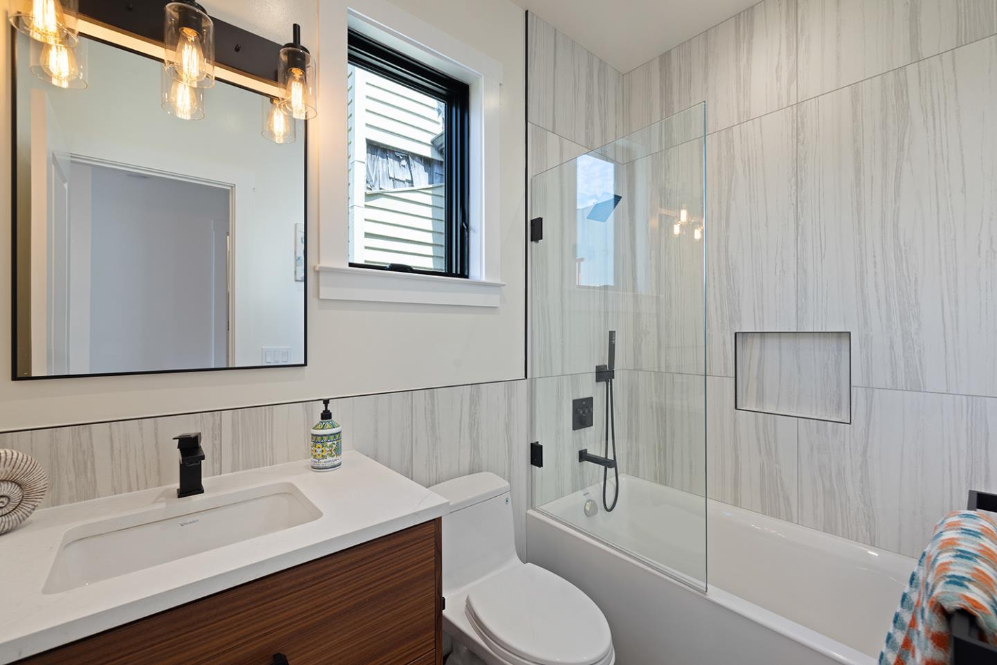 Modern bathroom with gray veined tile, a glass-enclosed tub, and a dark wood vanity.