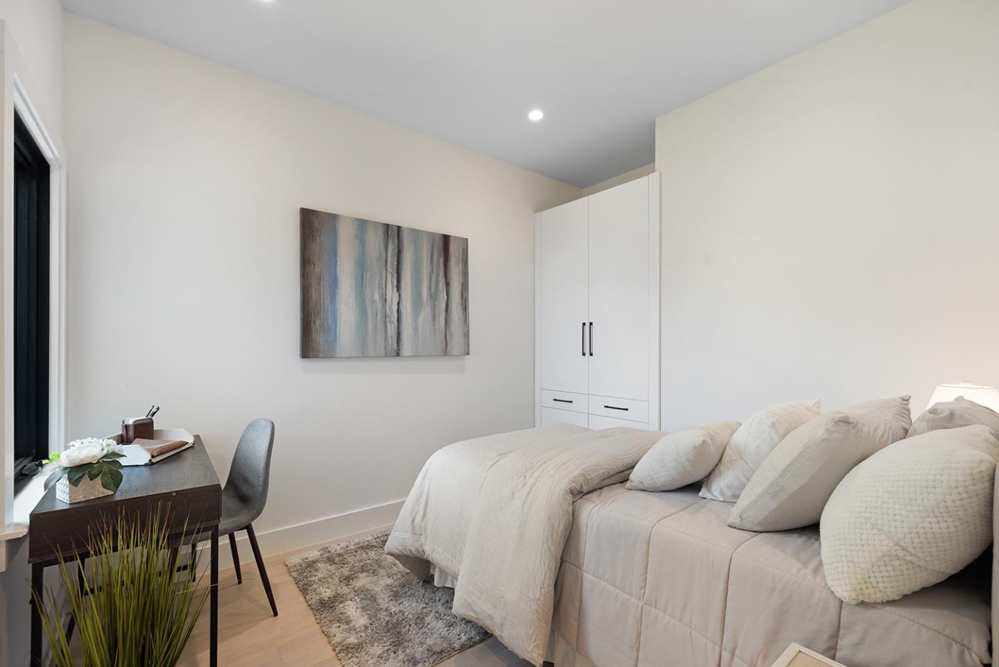 Staged bedroom with a white bed, built-in wardrobe, and desk beside a window.