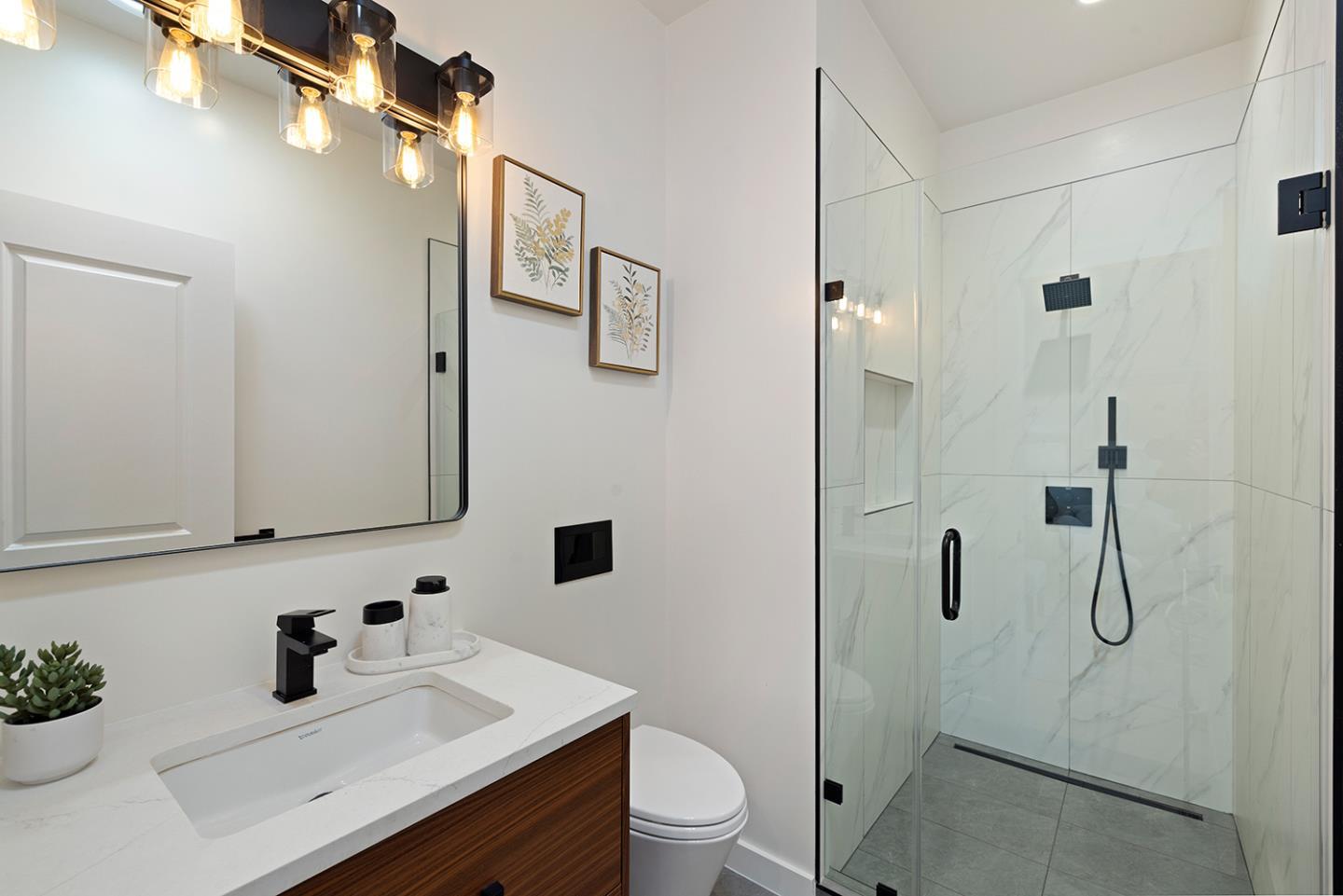 Modern bathroom with wood vanity, large mirror, and glass shower with black fixtures.