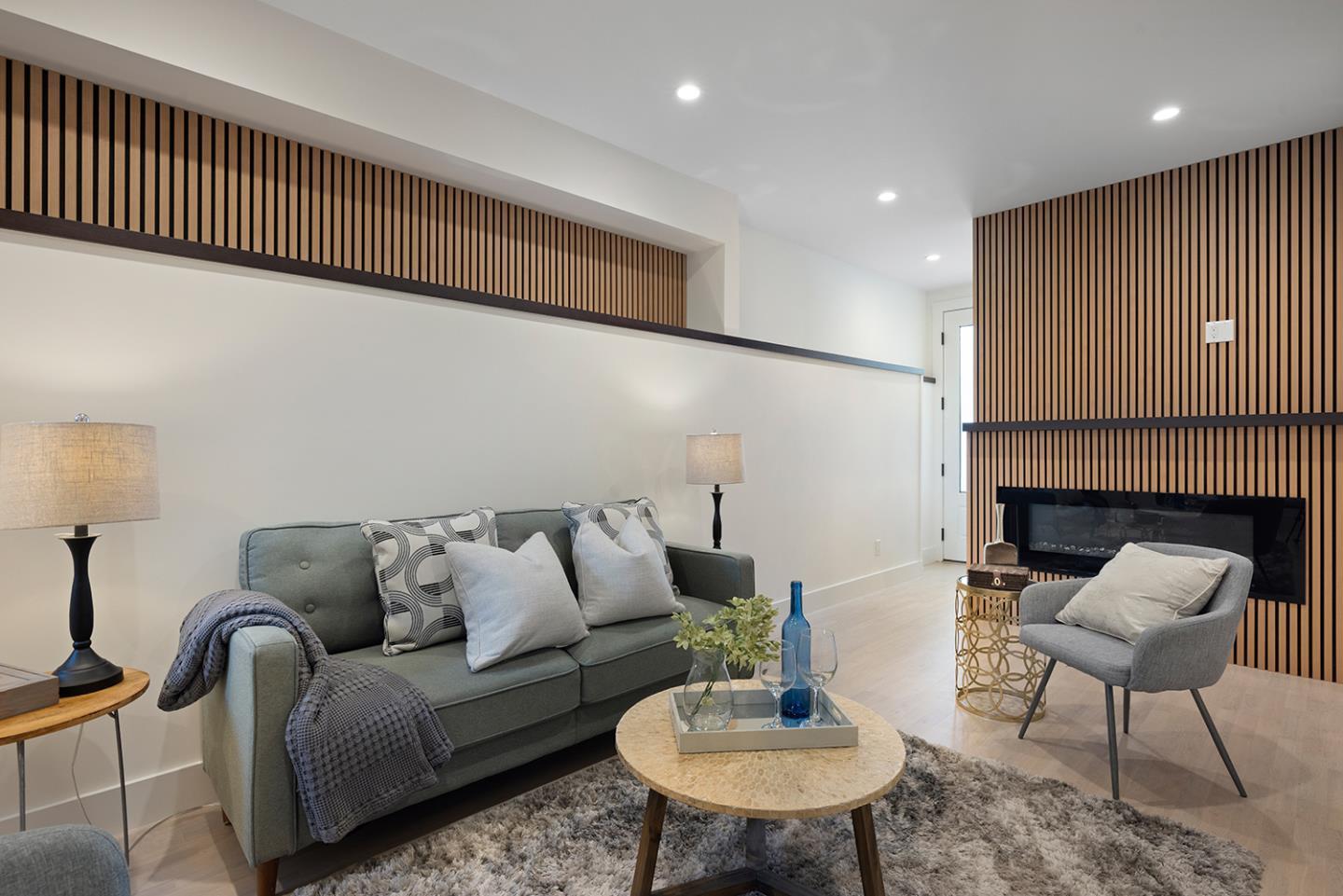 Staged living room with gray seating, a round coffee table, and a slatted wood fireplace wall.