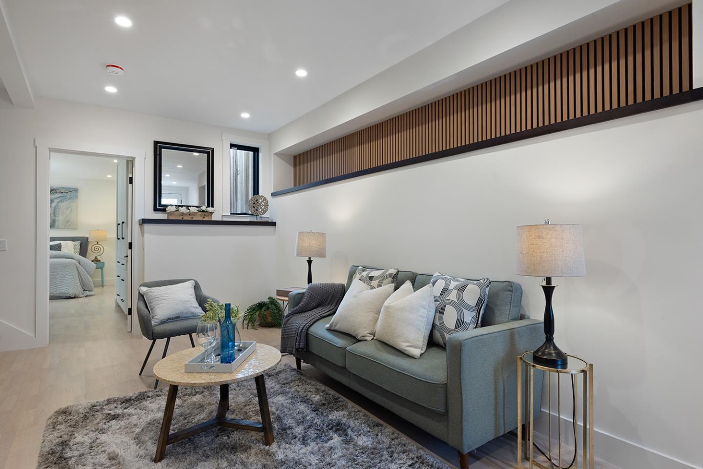 Staged living room with a gray-blue sofa, shag rug, and long wood-slat wall feature.