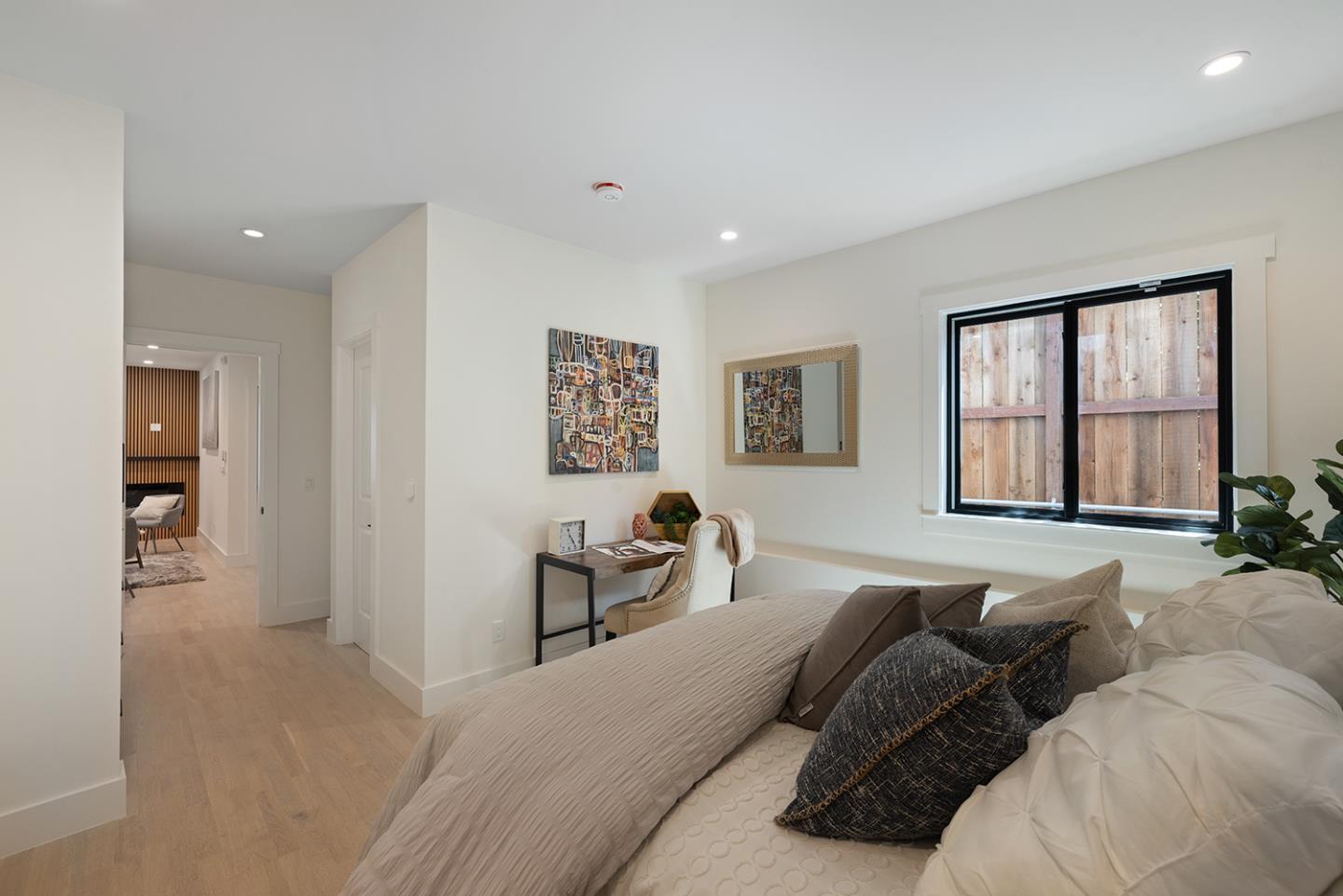Staged bedroom with a low bed, writing desk, and window facing a wooden fence.
