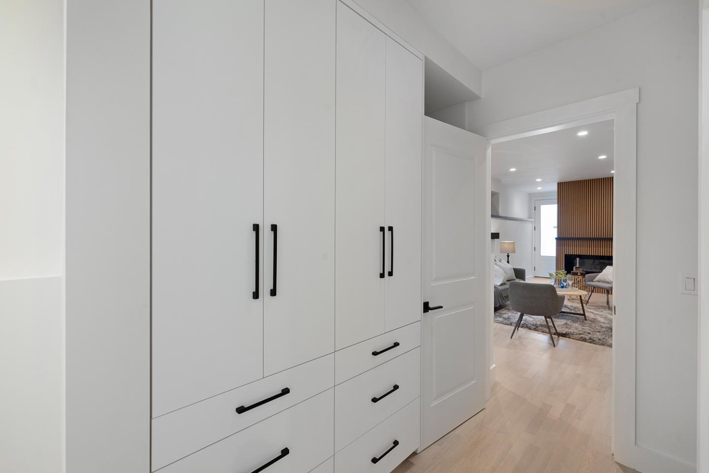 Hallway with built-in white cabinetry opens to a living room with a slatted wood feature wall.