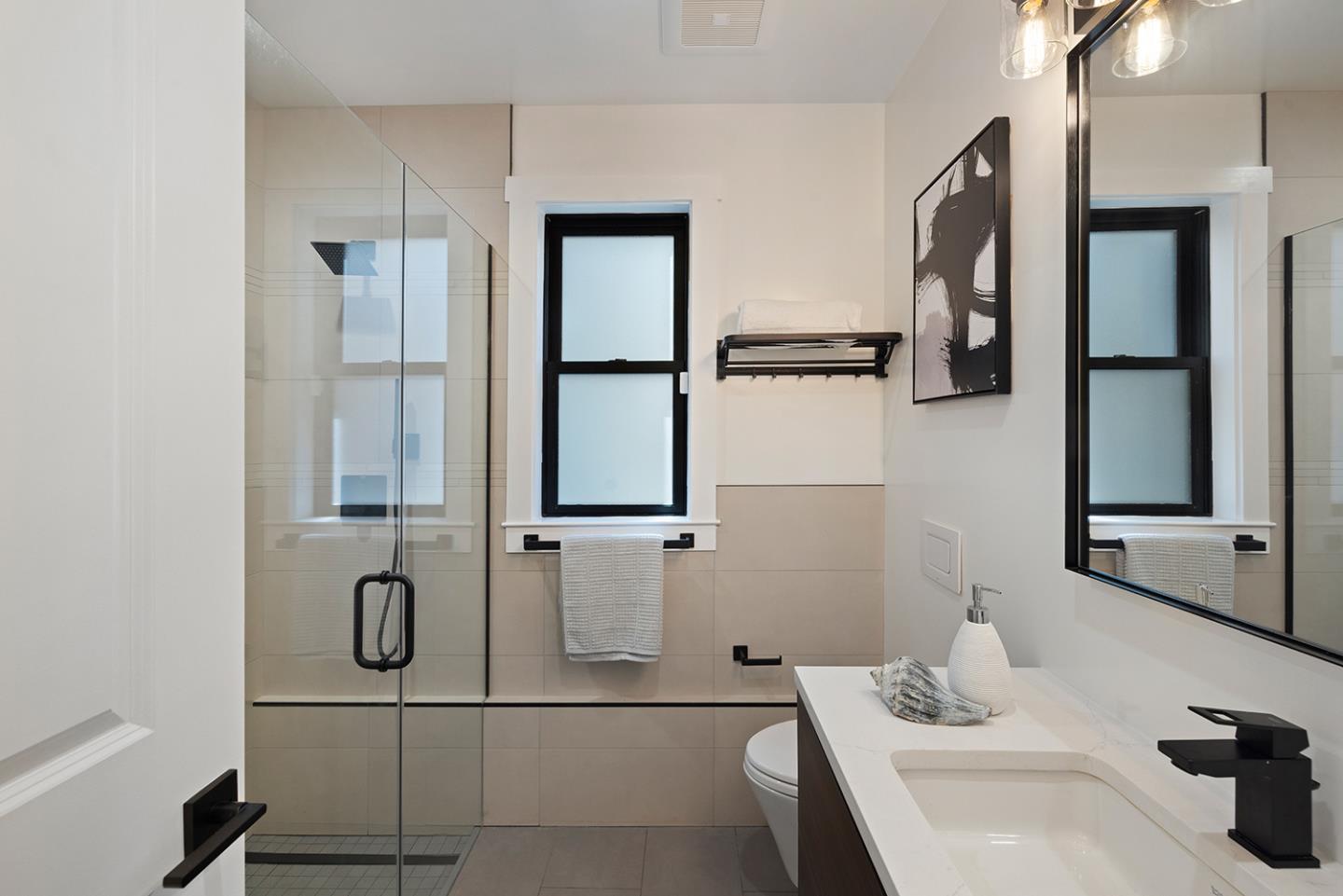 Modern bathroom with a glass shower, black-framed windows, and a white vanity.