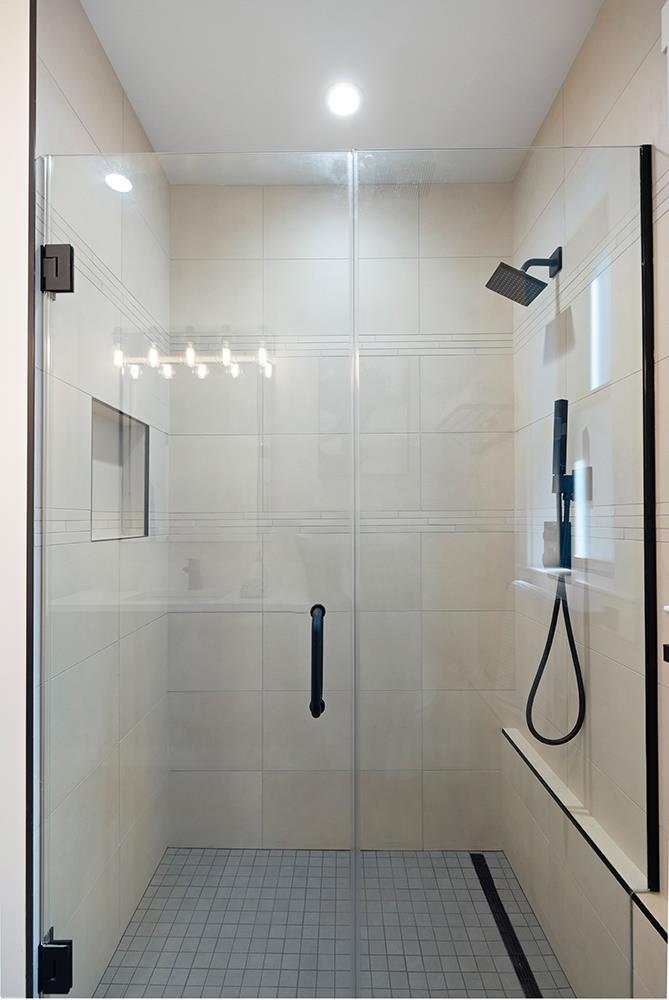 Walk-in shower with clear glass doors, light tile, black fixtures, and a built-in bench.
