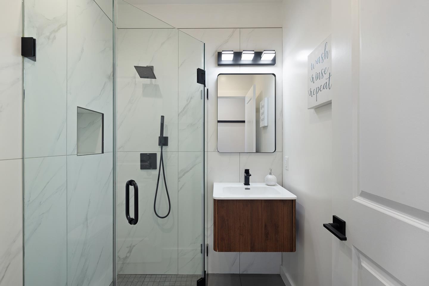 Modern bathroom with a marble-look glass shower, black fixtures, and a floating walnut vanity.