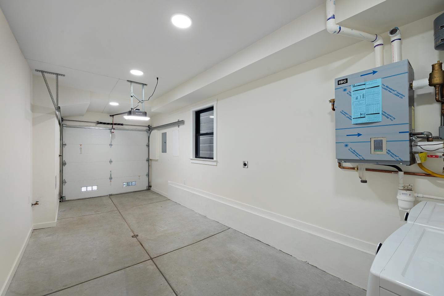 Empty garage with a concrete floor, closed garage door, small window, and wall-mounted heating unit.