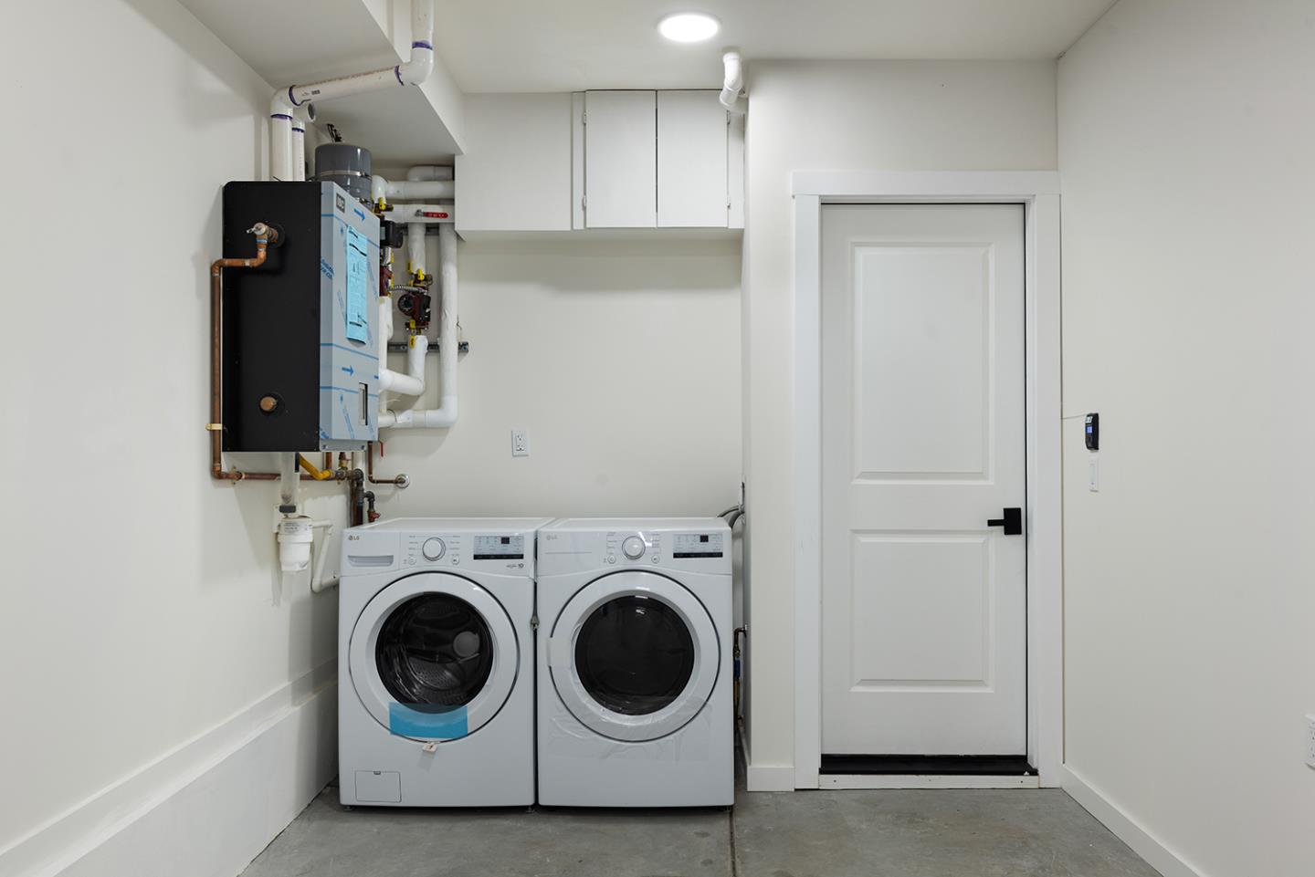 Laundry room with a front-loading washer and dryer, white cabinets, and a wall-mounted heating unit.